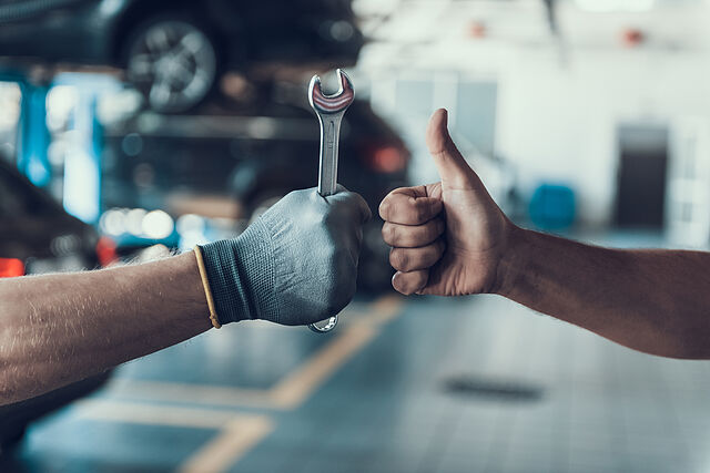 Close-up Thumb Up and Mechanics Hand with Tool. Automobile Master Wearing Gloves Showing Positive Gesture after Finishing Work. Technic occupation. Automobile Repair Service Concept.